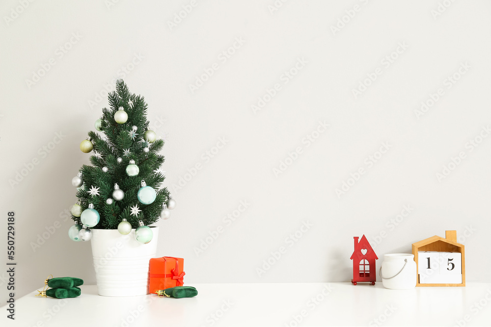 Small Christmas tree with toys on table near light wall