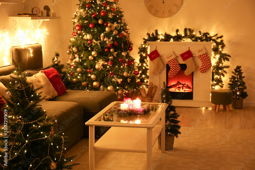 Interior of living room with sofa, glowing Christmas trees and fireplace at night