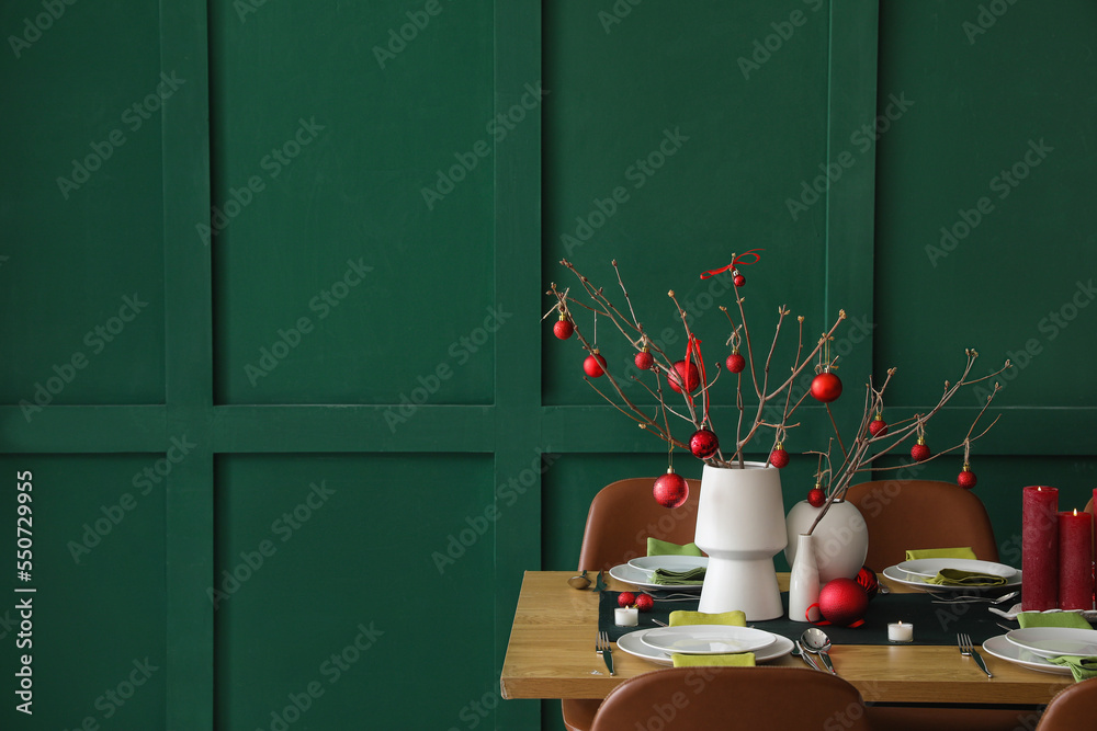 Vases with tree branches and red Christmas balls on dining table in room