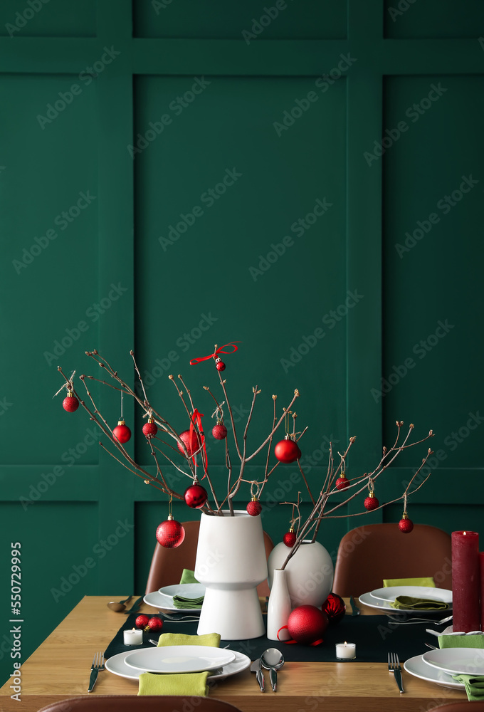 Vases with tree branches and red Christmas balls on dining table in room