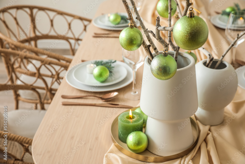 Vases with tree branches and green Christmas balls on dining table in room