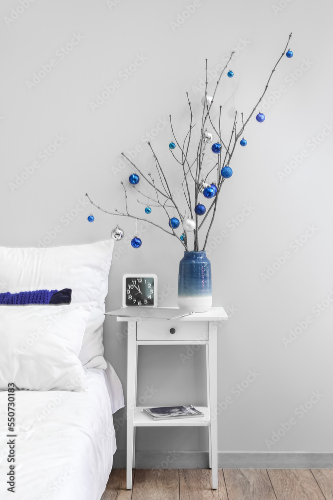 Vase with tree branches, Christmas balls and clock on table in bedroom