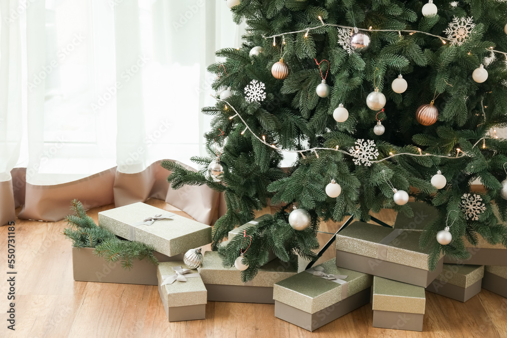 Decorated Christmas tree with presents near light curtain in living room