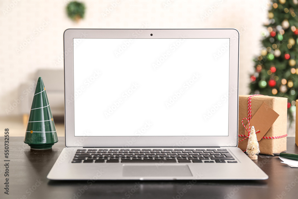 Laptop with Christmas trees and gift on table in office