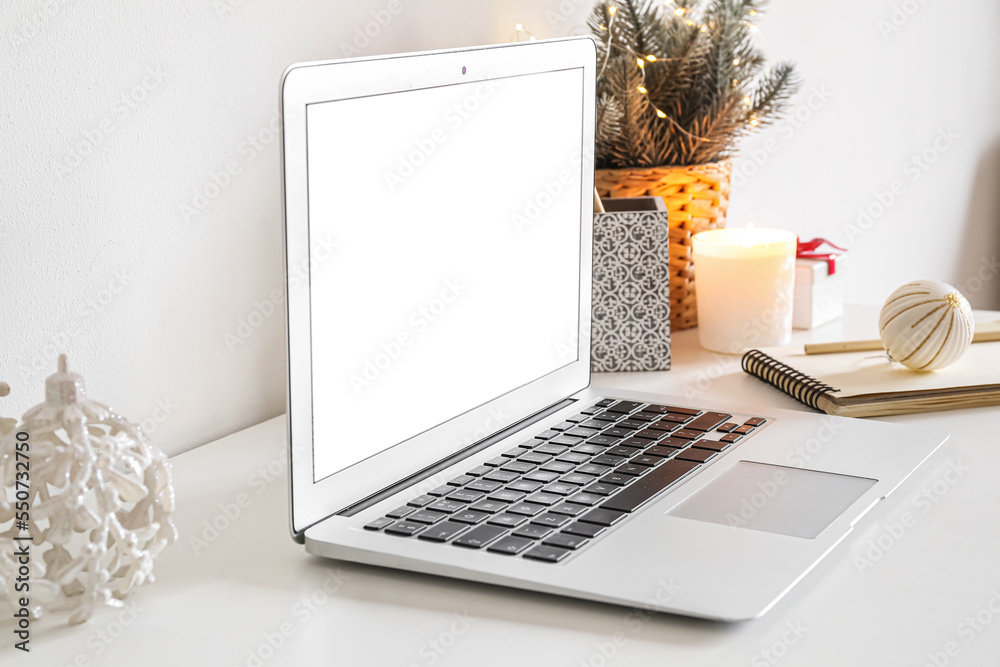 Laptop with candle and Christmas branches on table near white wall, closeup