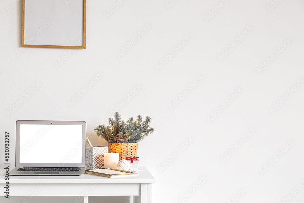 Workplace with laptop and Christmas branches near light wall