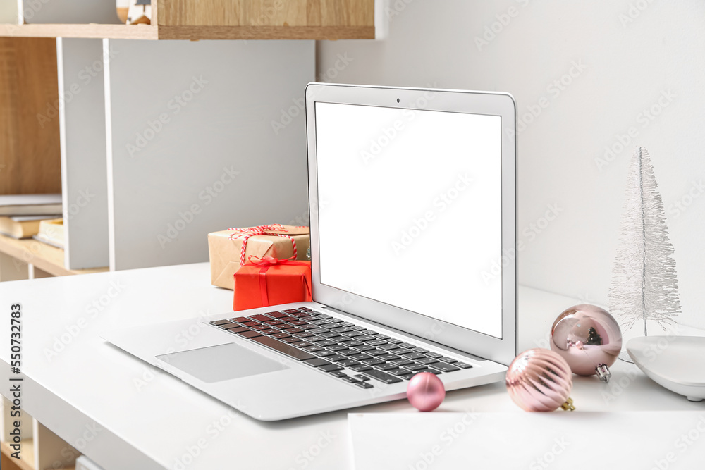 Laptop with Christmas gifts on table in office