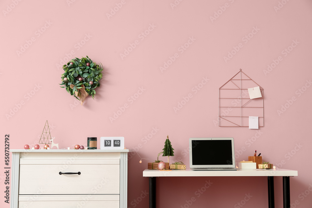 Workplace with laptop and Christmas gifts near pink wall in office