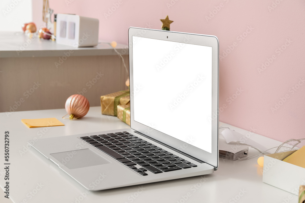 Laptop with Christmas gifts on table in office, closeup