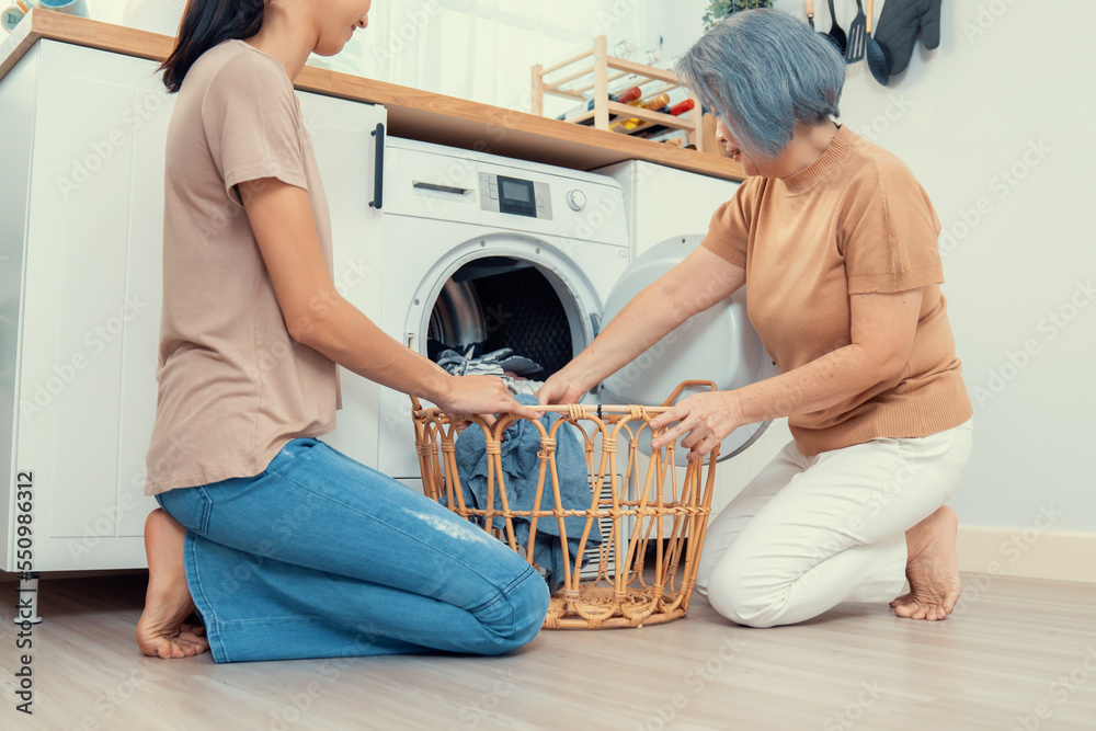 Daughter and mother working together to complete their household chores near the washing machine in 