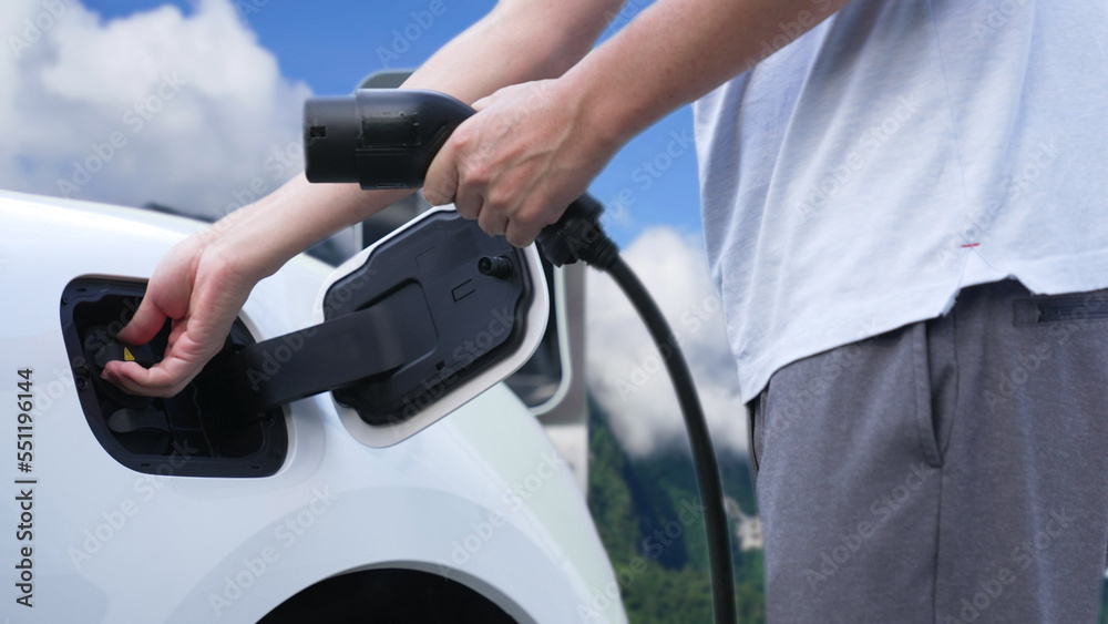 Progressive man recharge electric vehicle installing power cable plug from charging station with rur