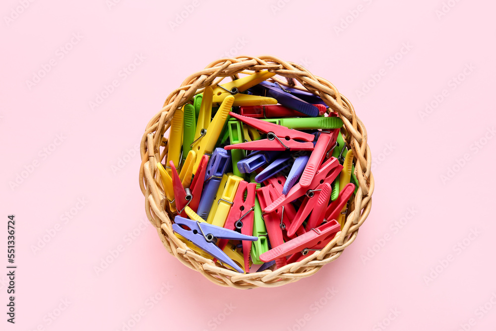 Basket with plastic clothespins on pink background