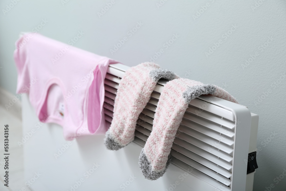 Warm socks and t-shirt drying on electric radiator near light wall, closeup