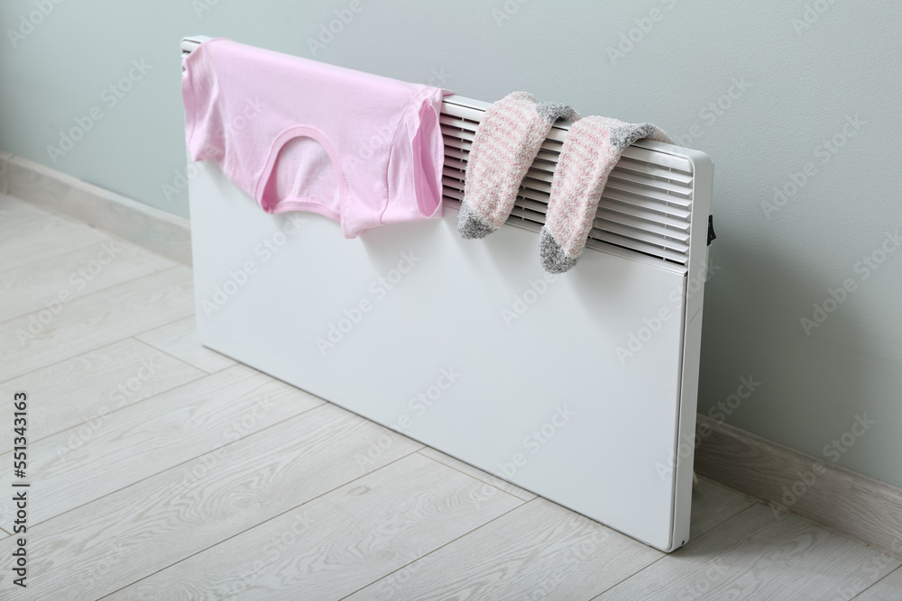 Warm socks and t-shirt drying on electric radiator near light wall