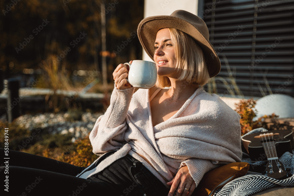 Beautiful woman in cowboy hat drinking coffee on patio in front of her house