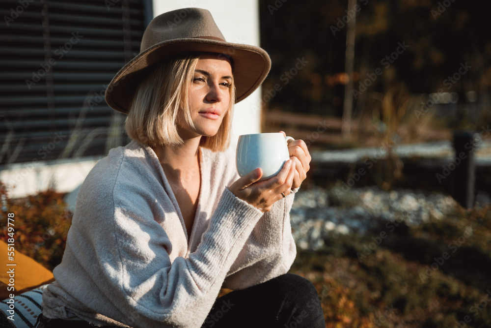 Beautiful woman in cowboy hat drinking coffee on patio in front of her house