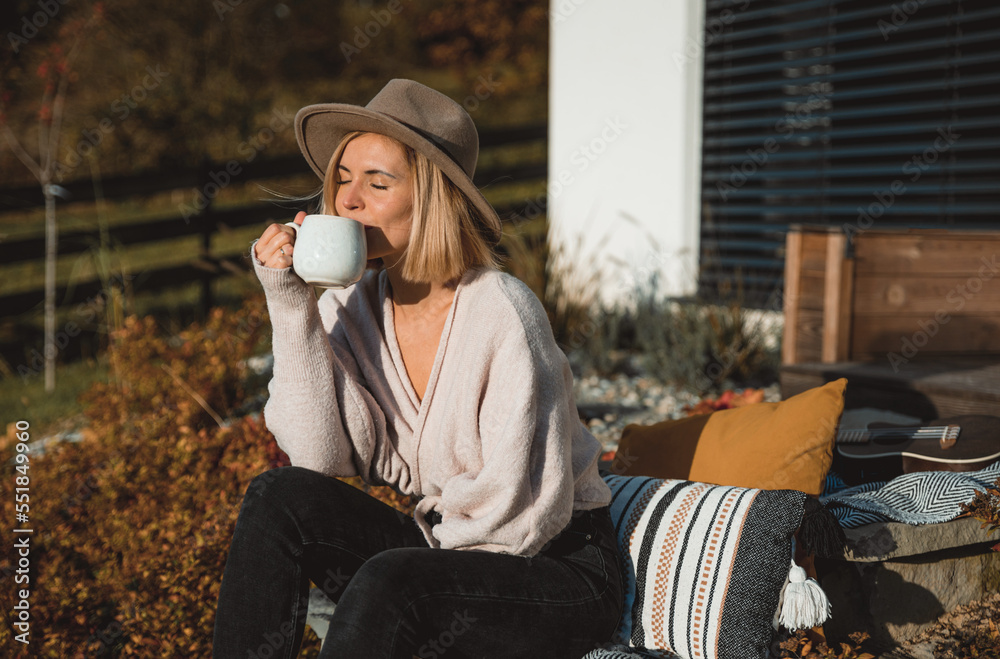 Beautiful woman in cowboy hat drinking coffee on patio in front of her house