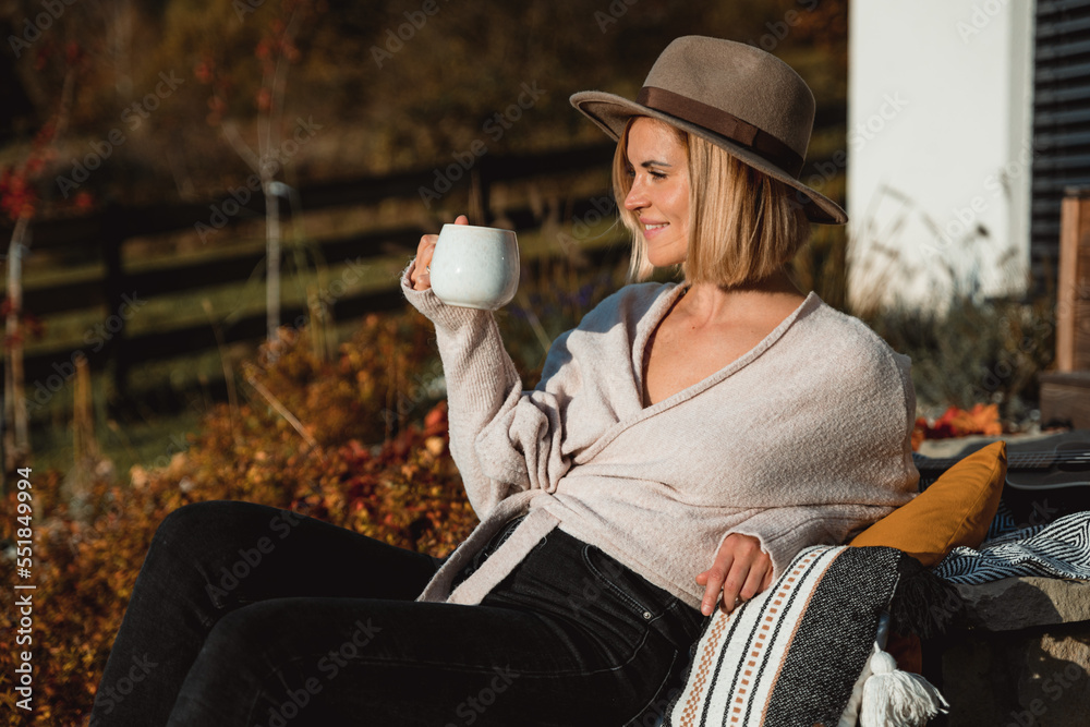 Beautiful woman in cowboy hat drinking coffee on patio in front of her house