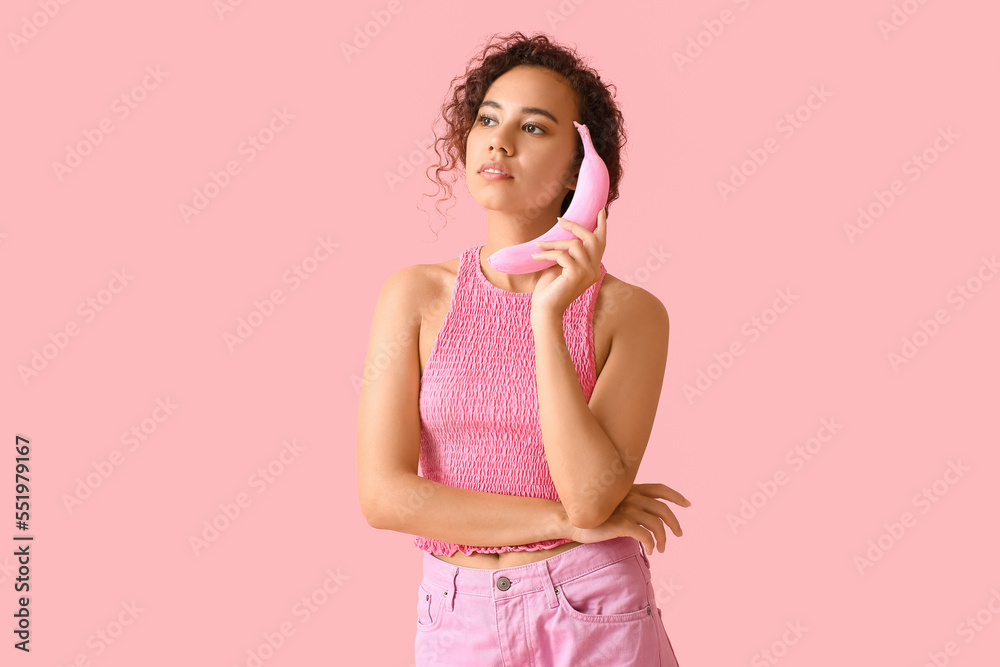 Beautiful African-American woman holding pink banana on color background