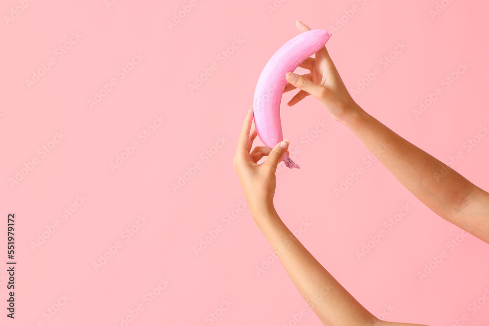 Female hands with pink banana on color background