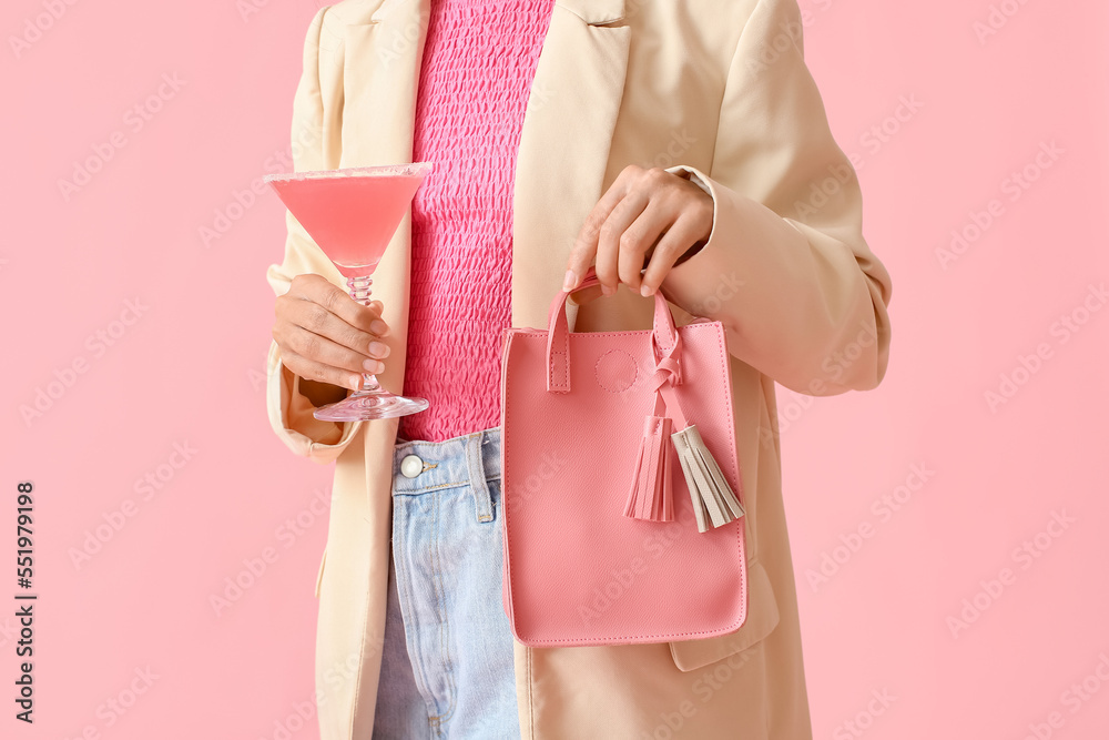 Woman holding pink lady cocktail and handbag on color background, closeup