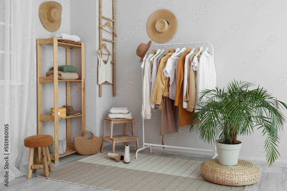 Interior of light dressing room with rack, clothes and shelving unit