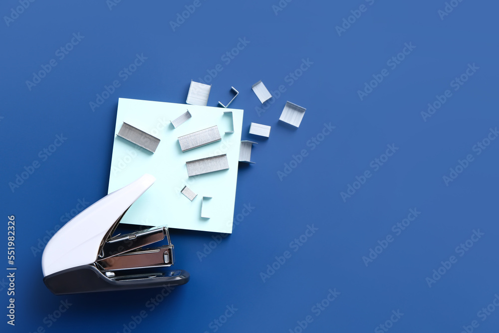 Stapler, staples and sticky notes on blue background