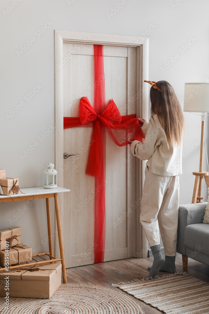 Young woman with red Christmas bow on wooden door in living room