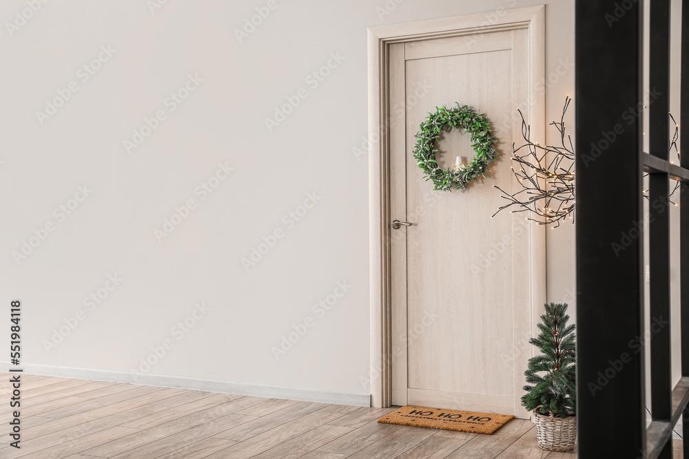 Wooden door with Christmas wreath, fir tree and lamp in hall