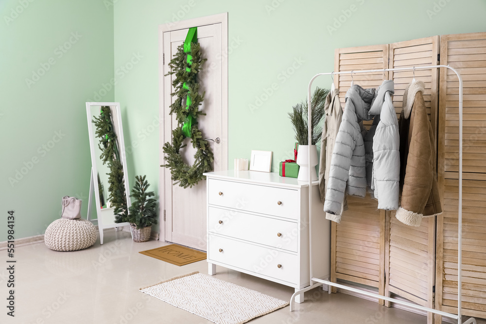 Interior of hall with wooden door, Christmas wreaths and jackets