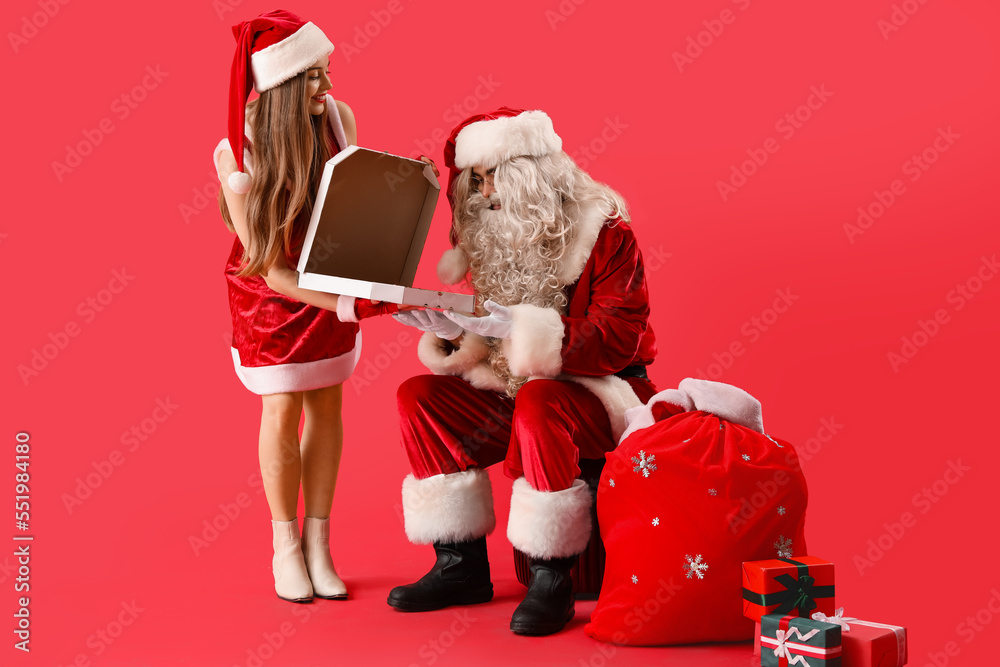 Young couple in Santa costumes eating tasty pizza on red background