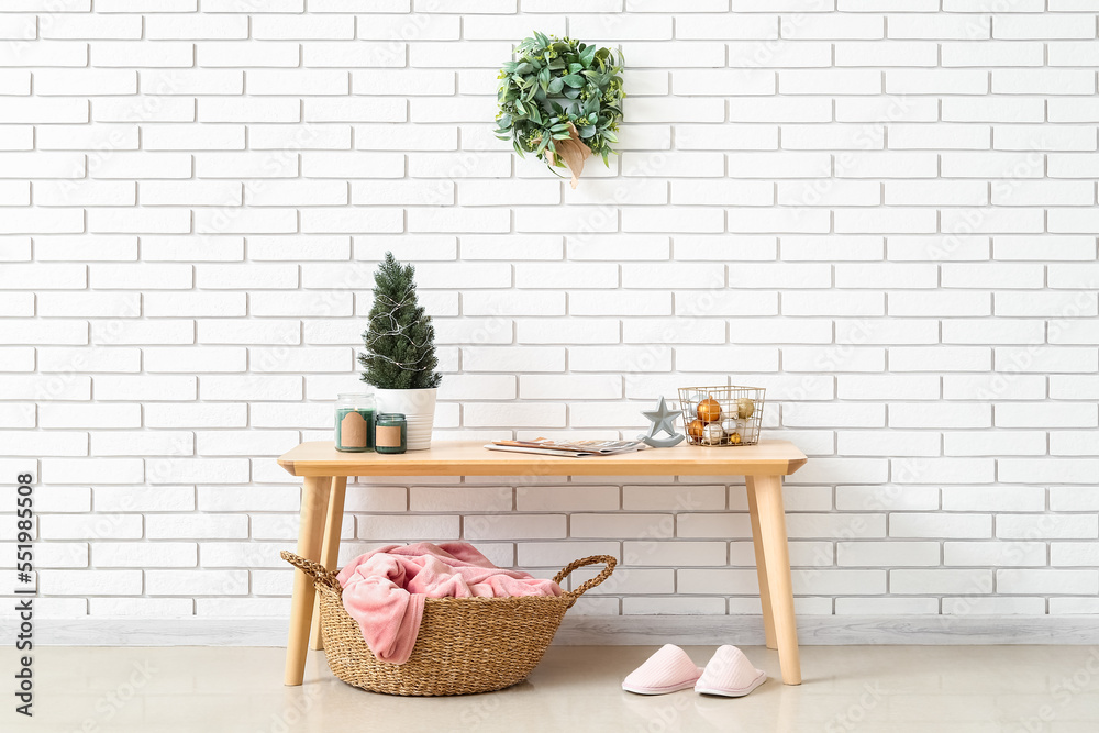 Table with fir tree, candles, Christmas balls and mistletoe wreath on white brick wall