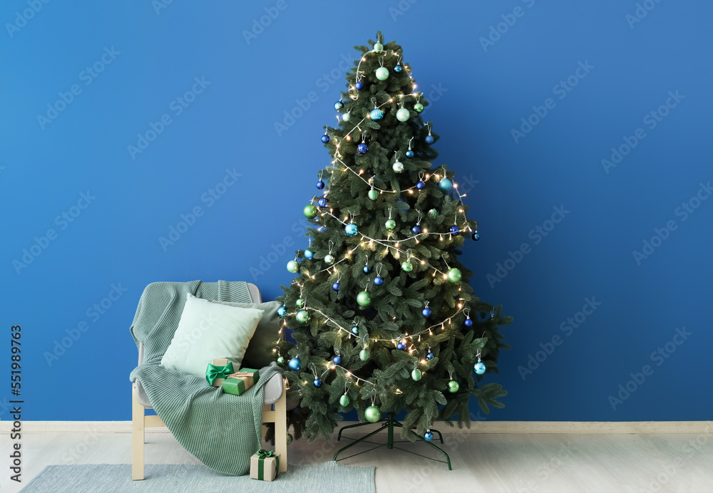 Glowing Christmas tree and chair with presents near blue wall