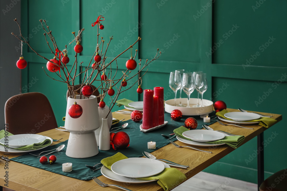 Vases with tree branches and red Christmas balls on dining table in room