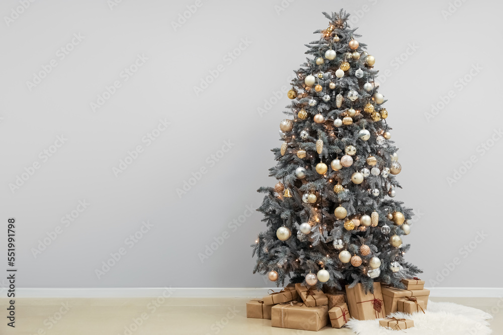 Glowing Christmas tree with presents near grey wall