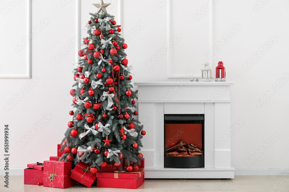 Decorated Christmas tree with presents and fireplace near light wall