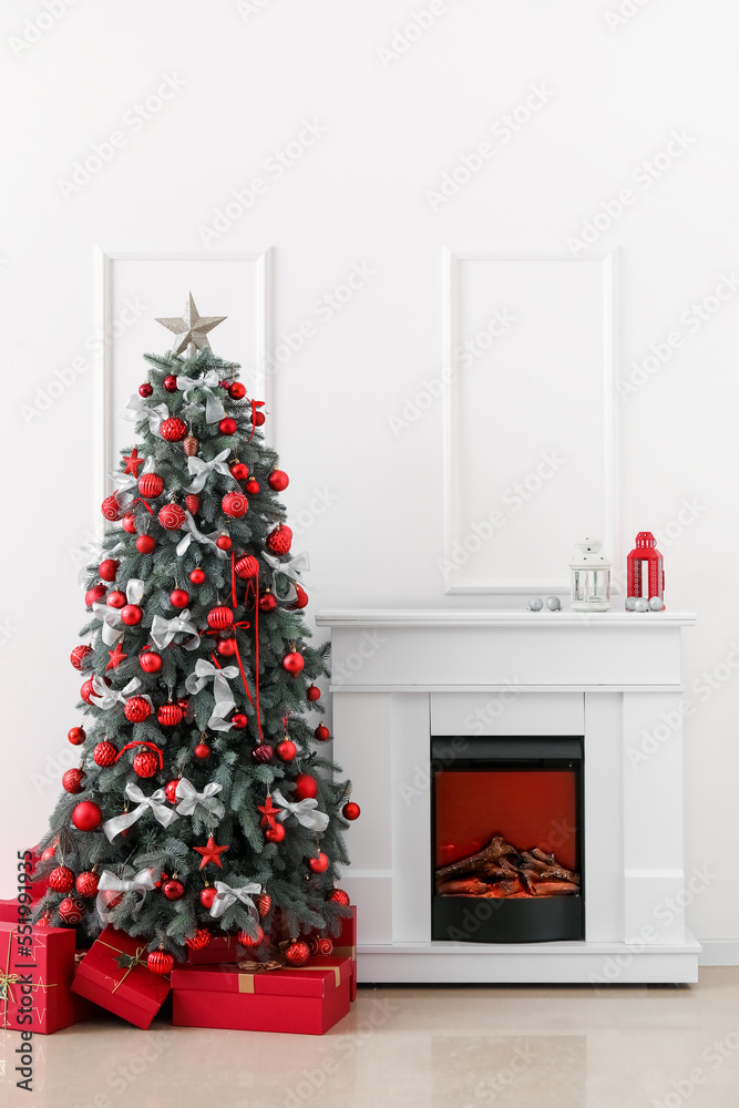 Decorated Christmas tree with presents and fireplace near light wall