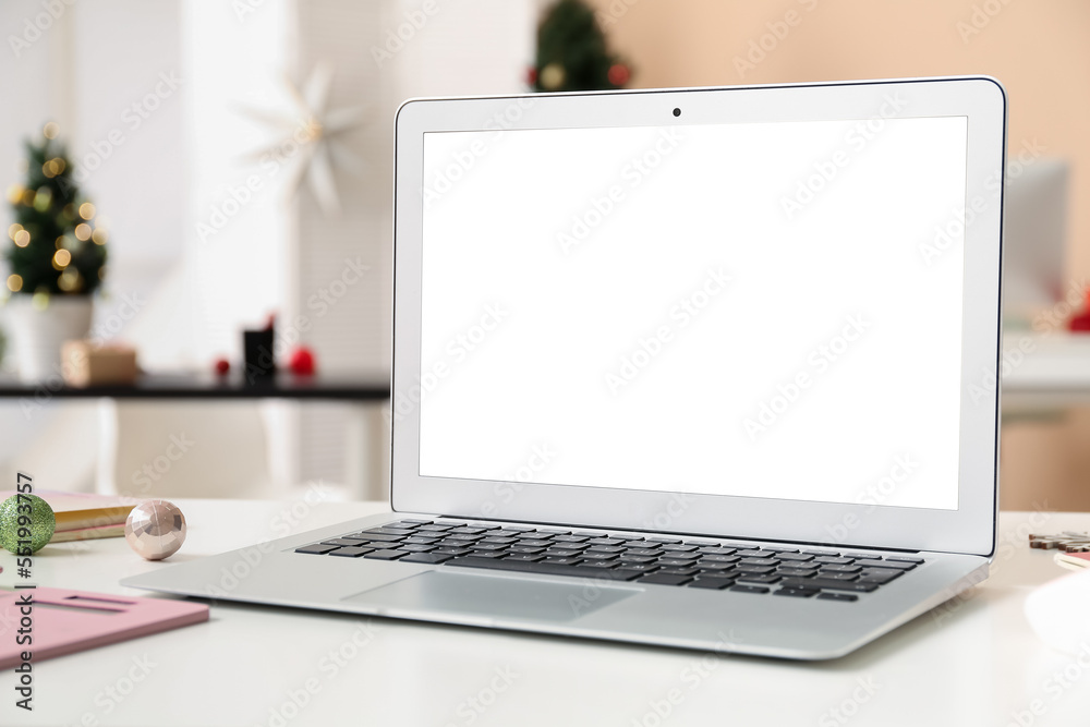 Laptop with Christmas balls on table in office, closeup