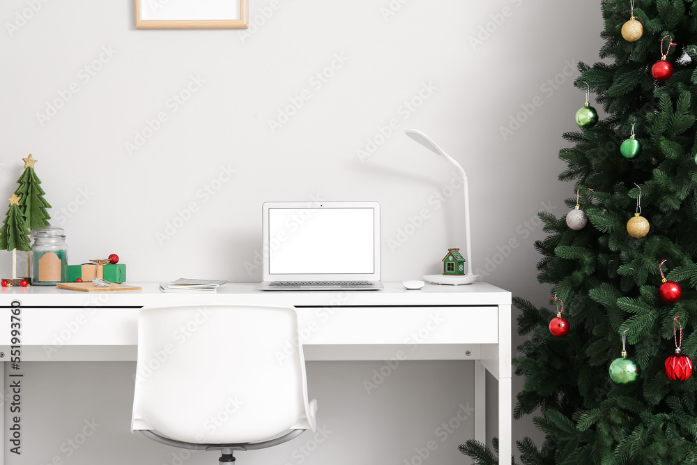 Workplace with laptop, Christmas tree, gift and candle near light wall in office