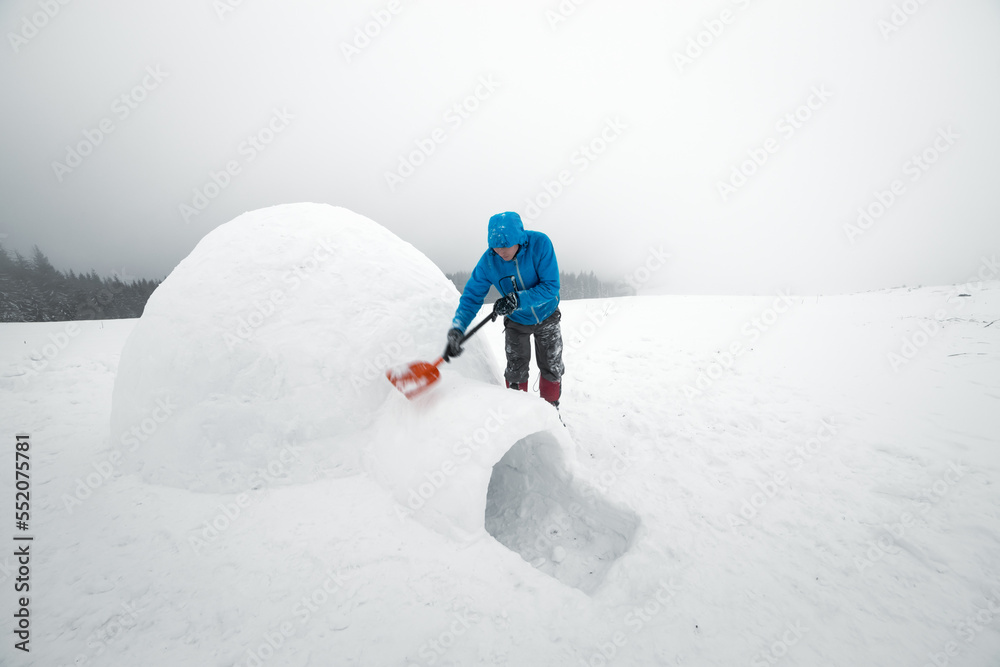 Man in blue jacket building igloo in the high mountain. Fantastic winter scene