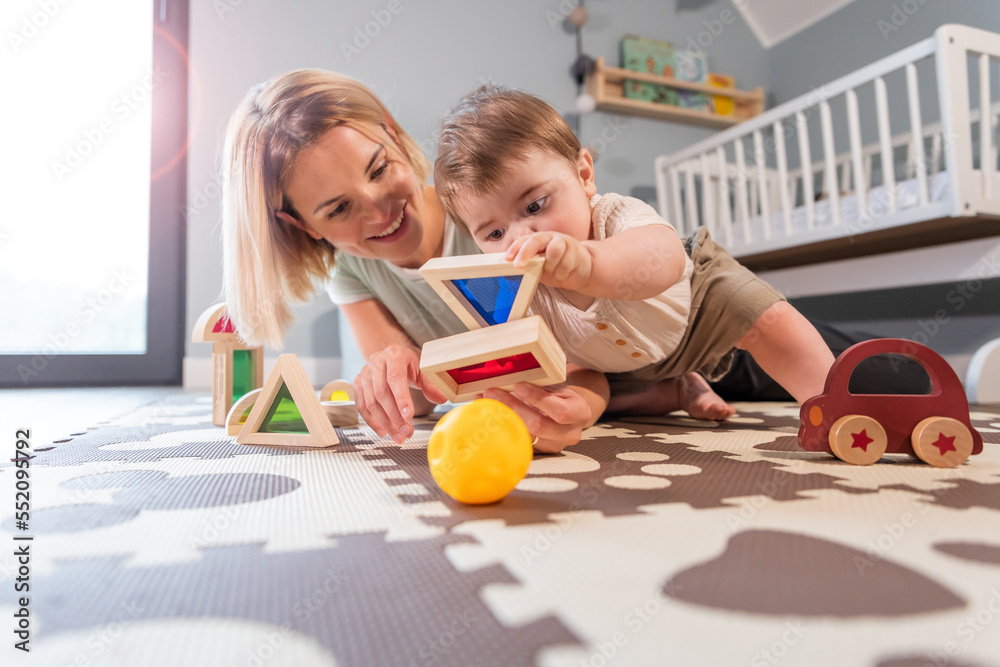 Loving family mom and baby boy playing together toys on floor in child room