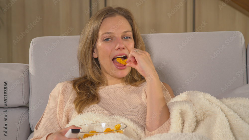 CLOSE UP: Relaxed woman munching on chips and watching entertaining TV program