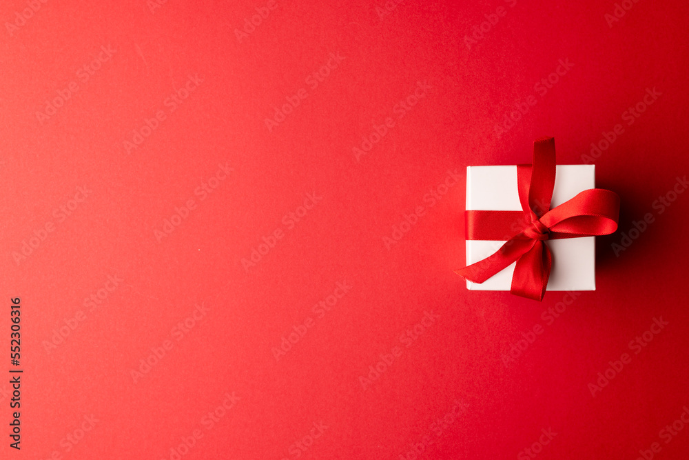 Overhead of white gift box tied with red ribbon, on red background with copy space