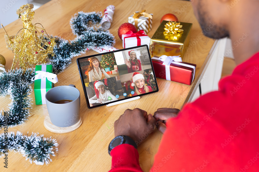 African american man with christmas decorations having video call with happy caucasian friends