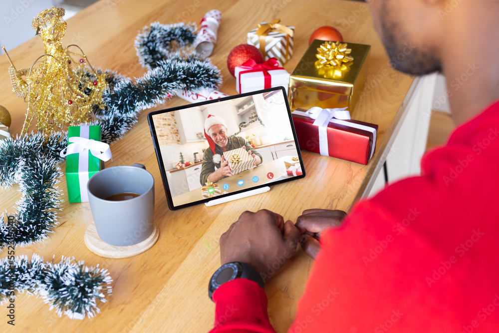 African american man with christmas decorations having video call with happy caucasian man