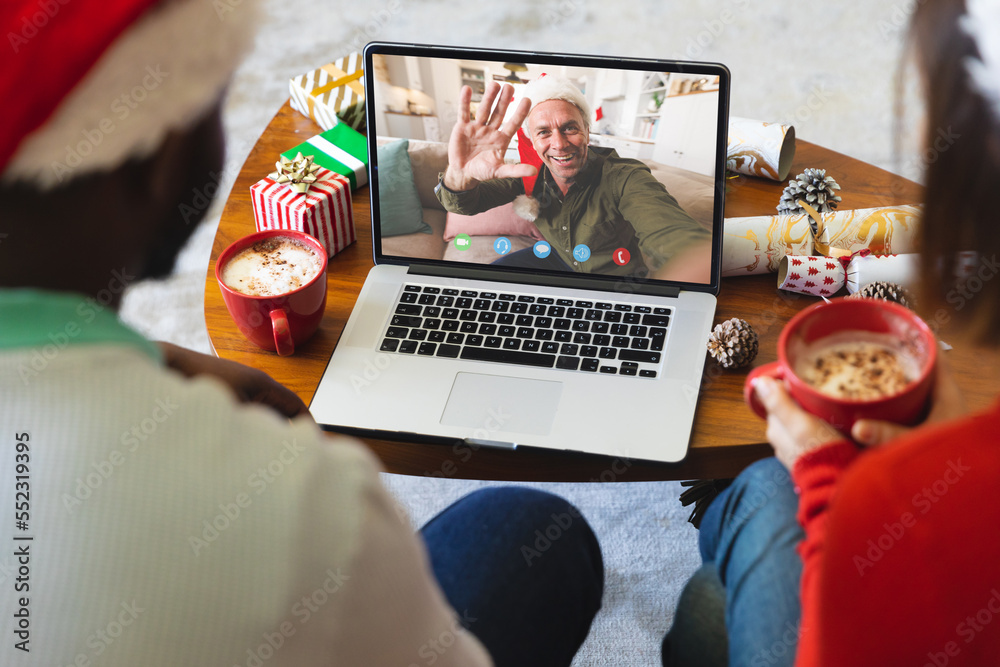 Diverse couple with christmas decorations having video call with happy caucasian man