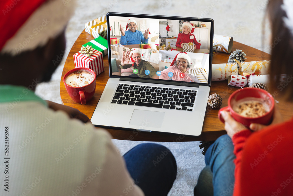 Diverse couple with christmas decorations having video call with happy diverse friends