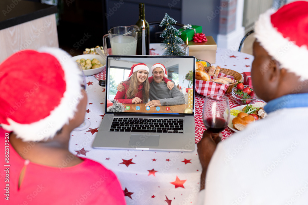 African american couple with santa hats having video call with happy caucasian family