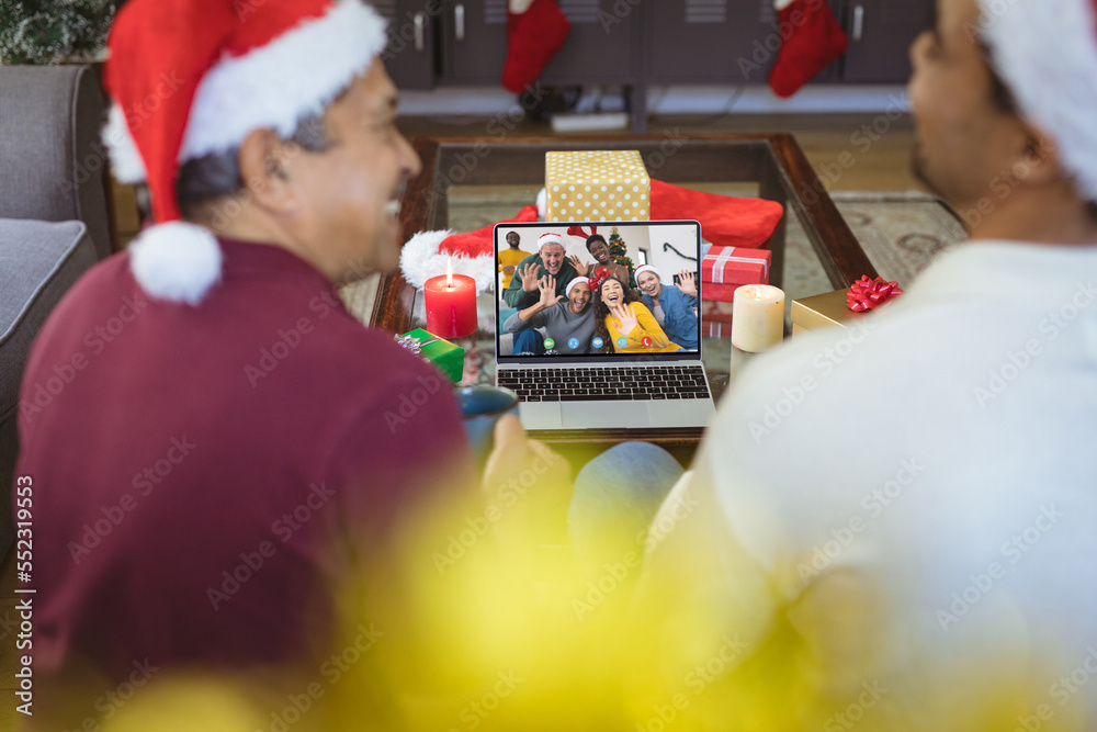 Biracial father and adult son with santa hats having video call with happy diverse friends