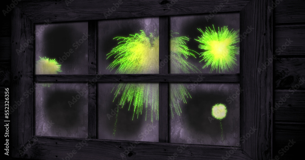 Image of window with green christmas and new year fireworks exploding in night sky